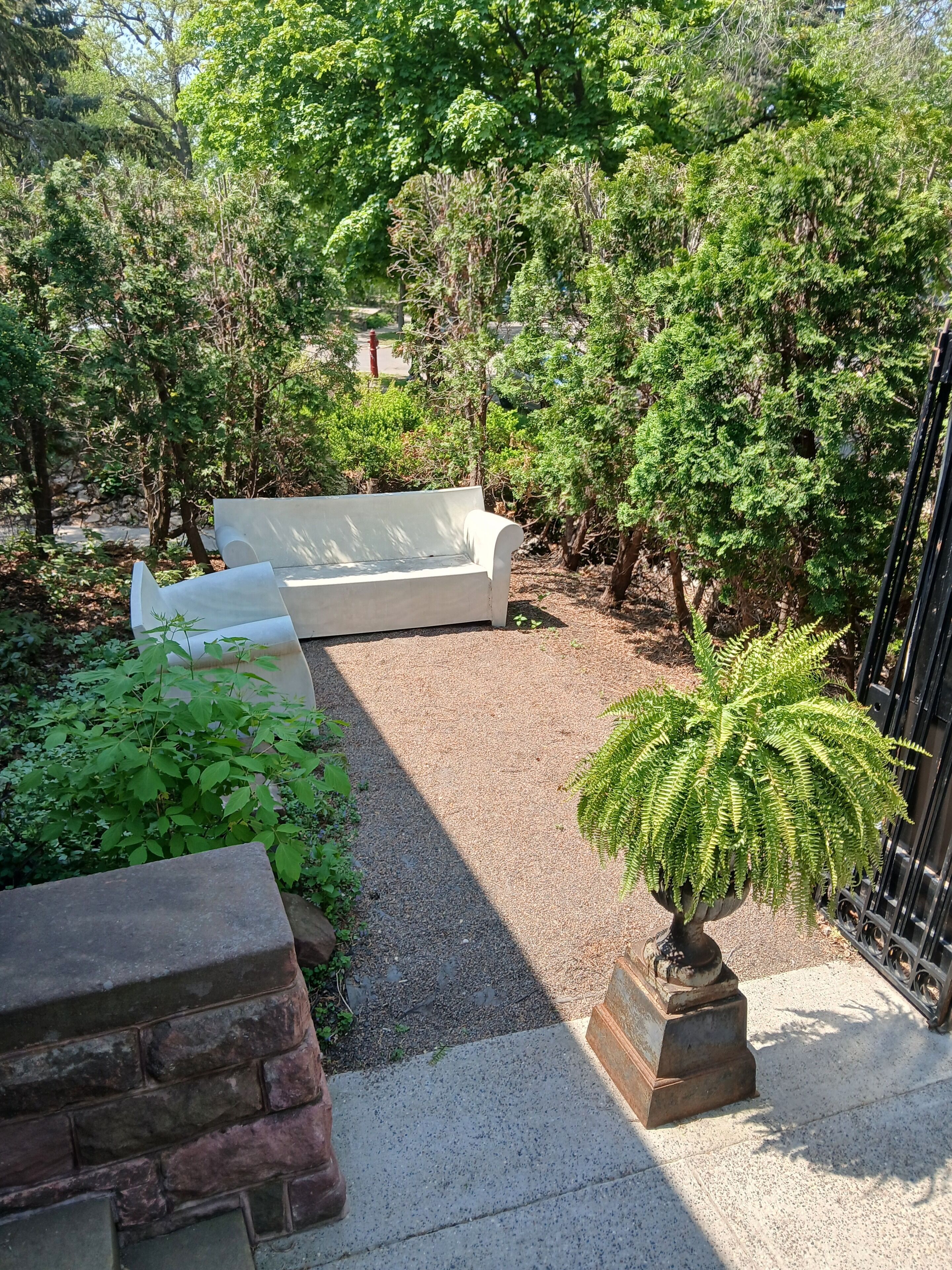 Un'area giardino con una panchina bianca, un vaso con felce e un muro in pietra.
