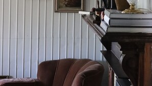 Una habitació amb una butaca marró, una llar de foc amb un ram i obra d'art amb marc a la paret.