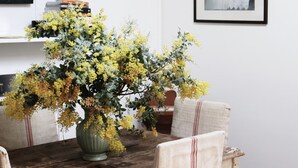 Taula de menjador amb un ram de flors grogues, una làmpada i un quadre al mur.