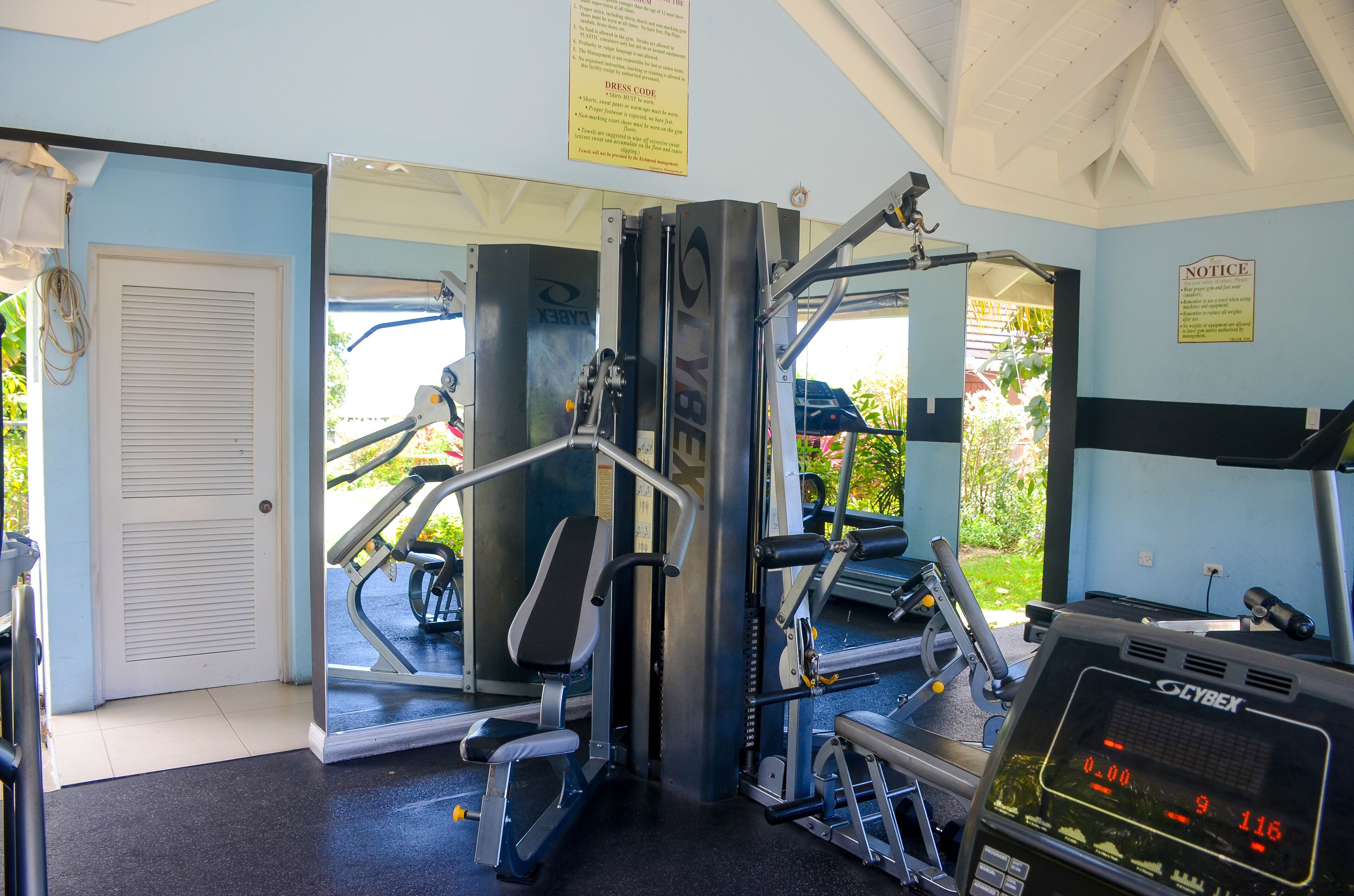 Une salle de sport équipée de matériel d’exercice, dotée d’un écran numérique et d’une porte donnant sur l’extérieur.