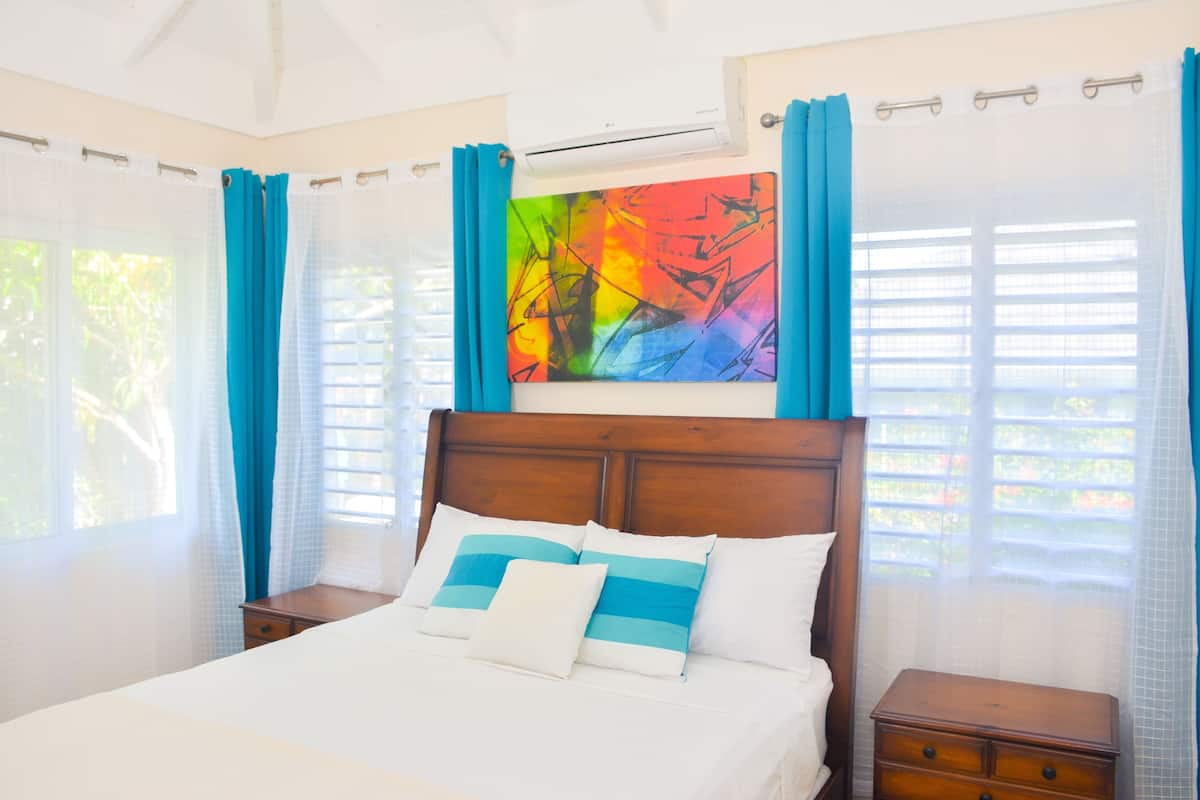 A bedroom with a wooden headboard, a bed with white and blue striped pillows, a nightstand, and a colorful abstract painting above the bed.