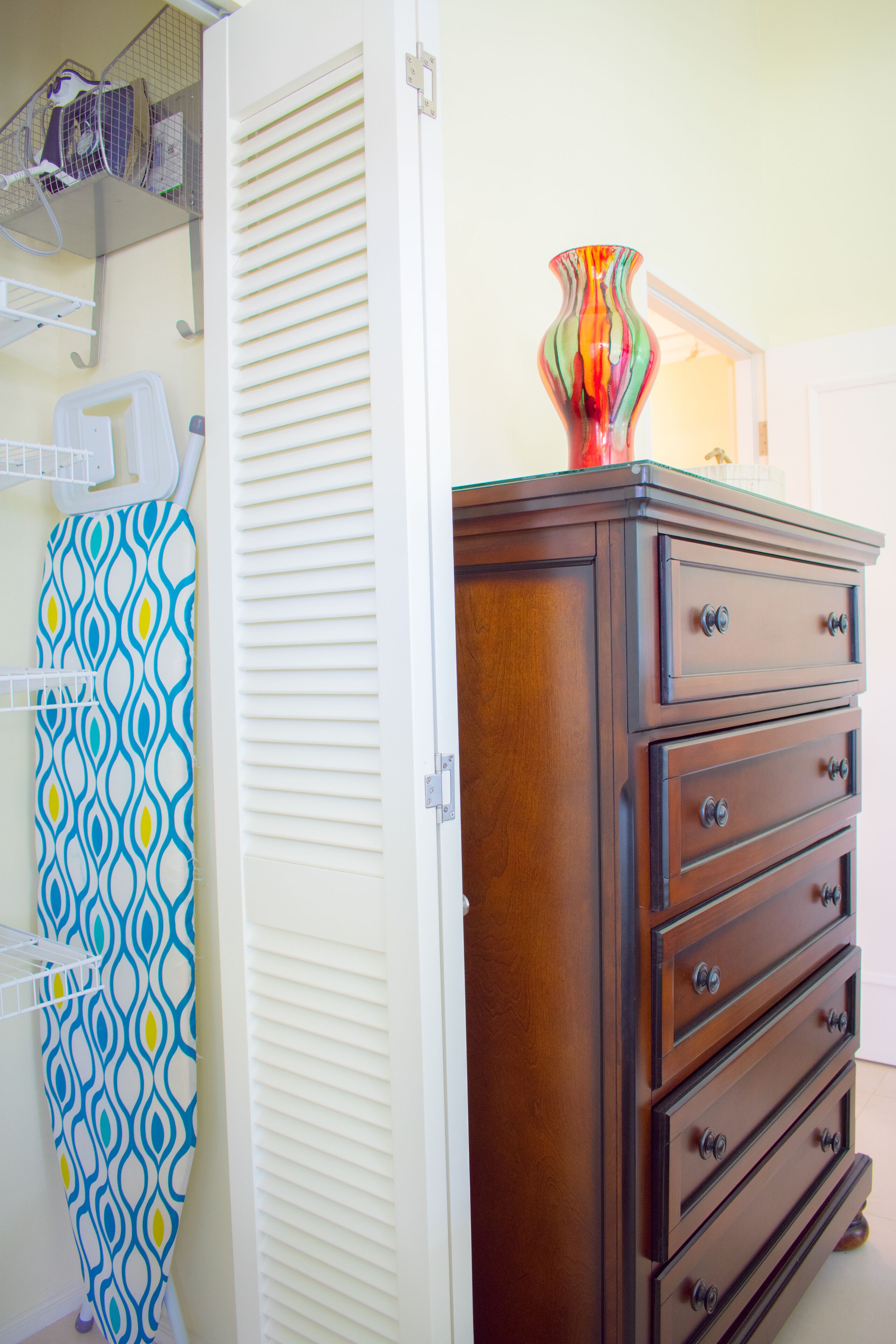 A wooden dresser with multiple drawers and a colorful vase on top.