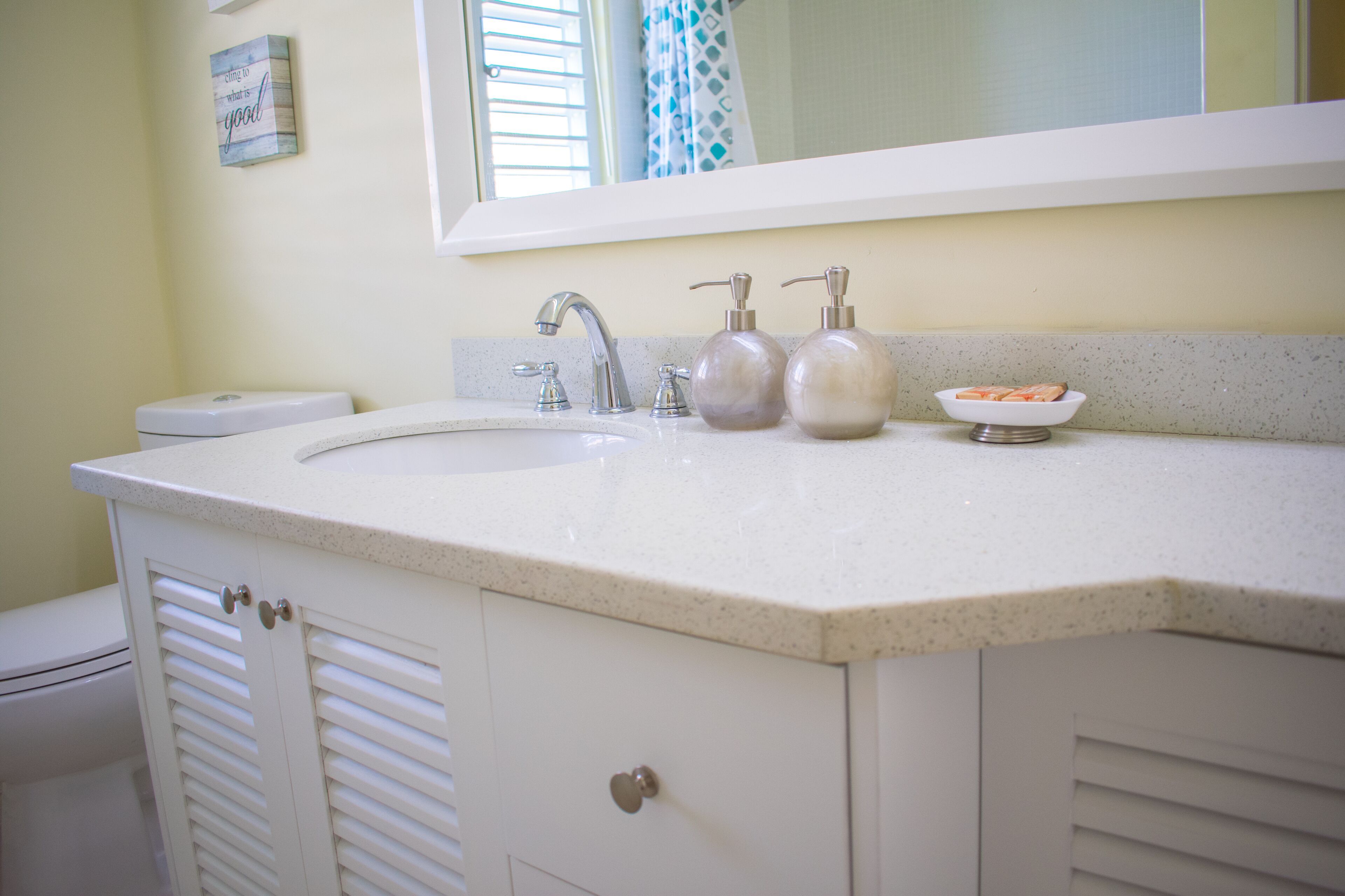A bathroom with a white sink, two soap dispensers, a mirror above the sink, and a toilet to the left.