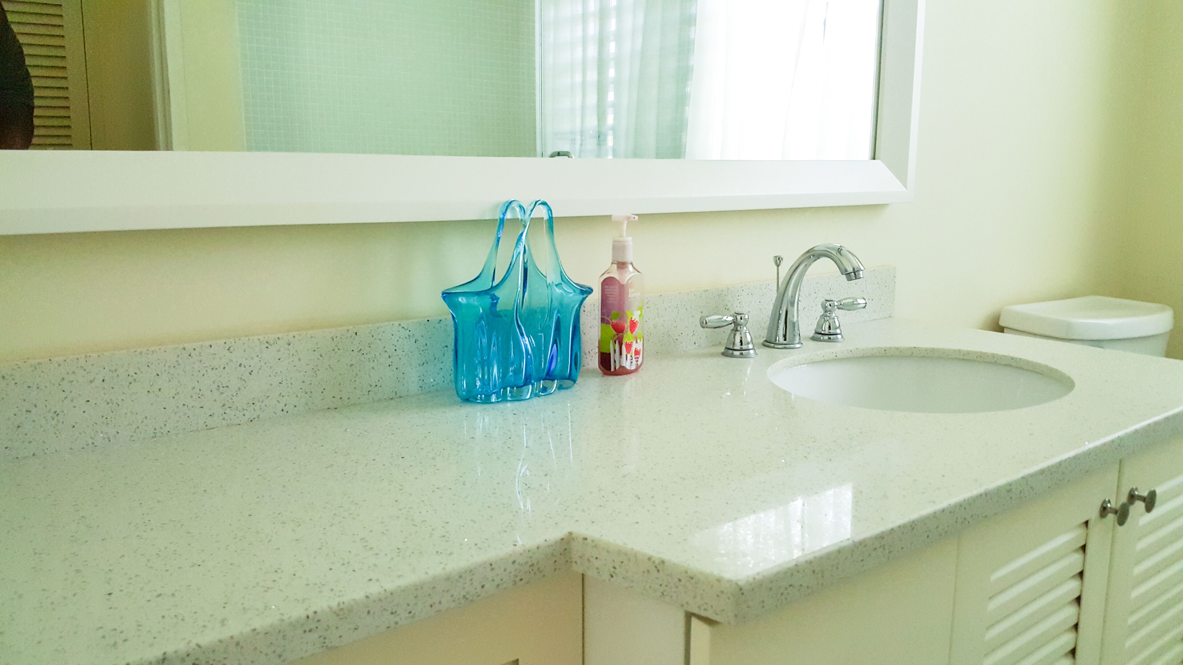 Un baño con un lavamanos blanco, un espejo encima y un dispensador de jabón de vidrio azul.