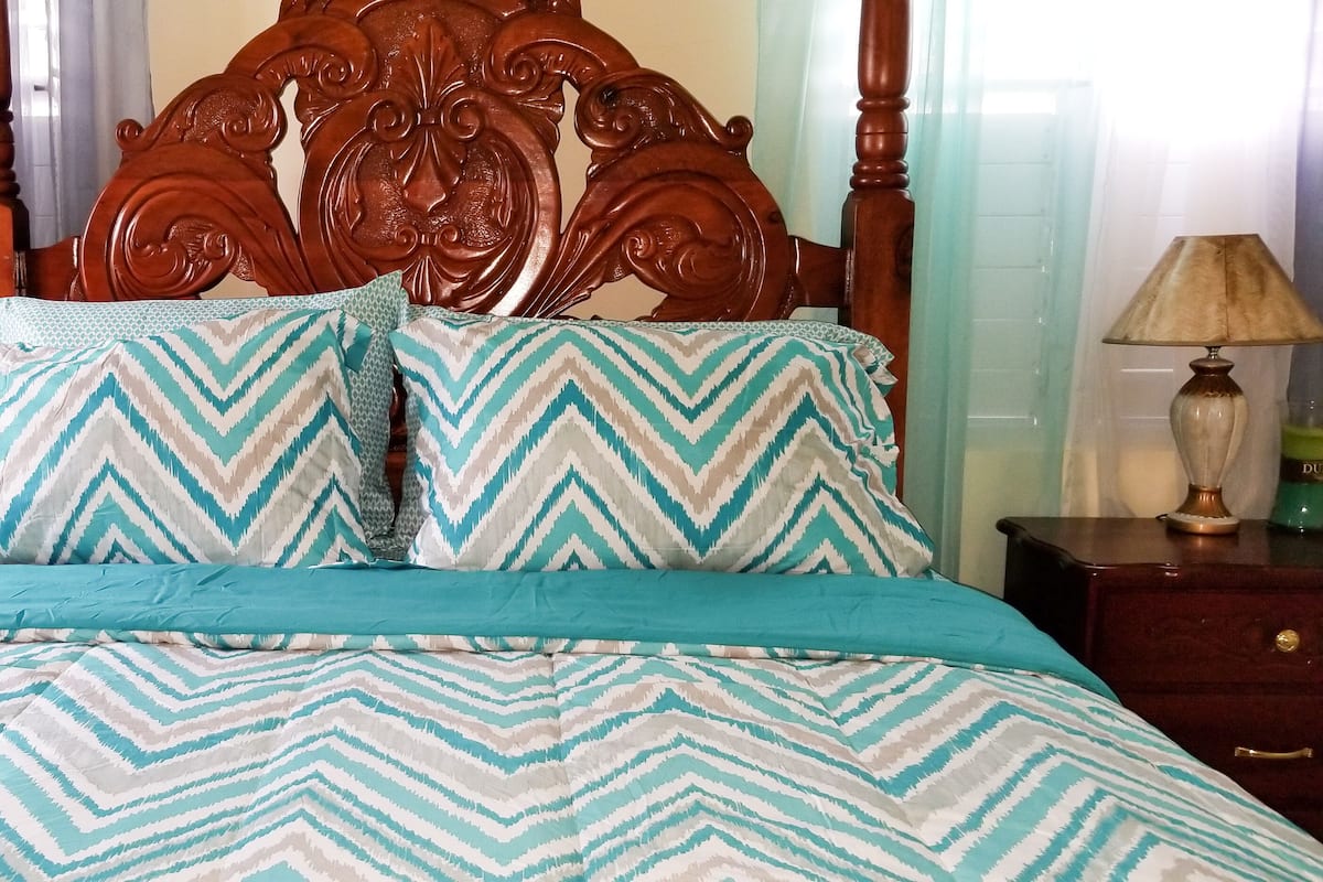 A bed with a patterned bedspread and pillows, a wooden headboard, and two bedside tables with lamps.