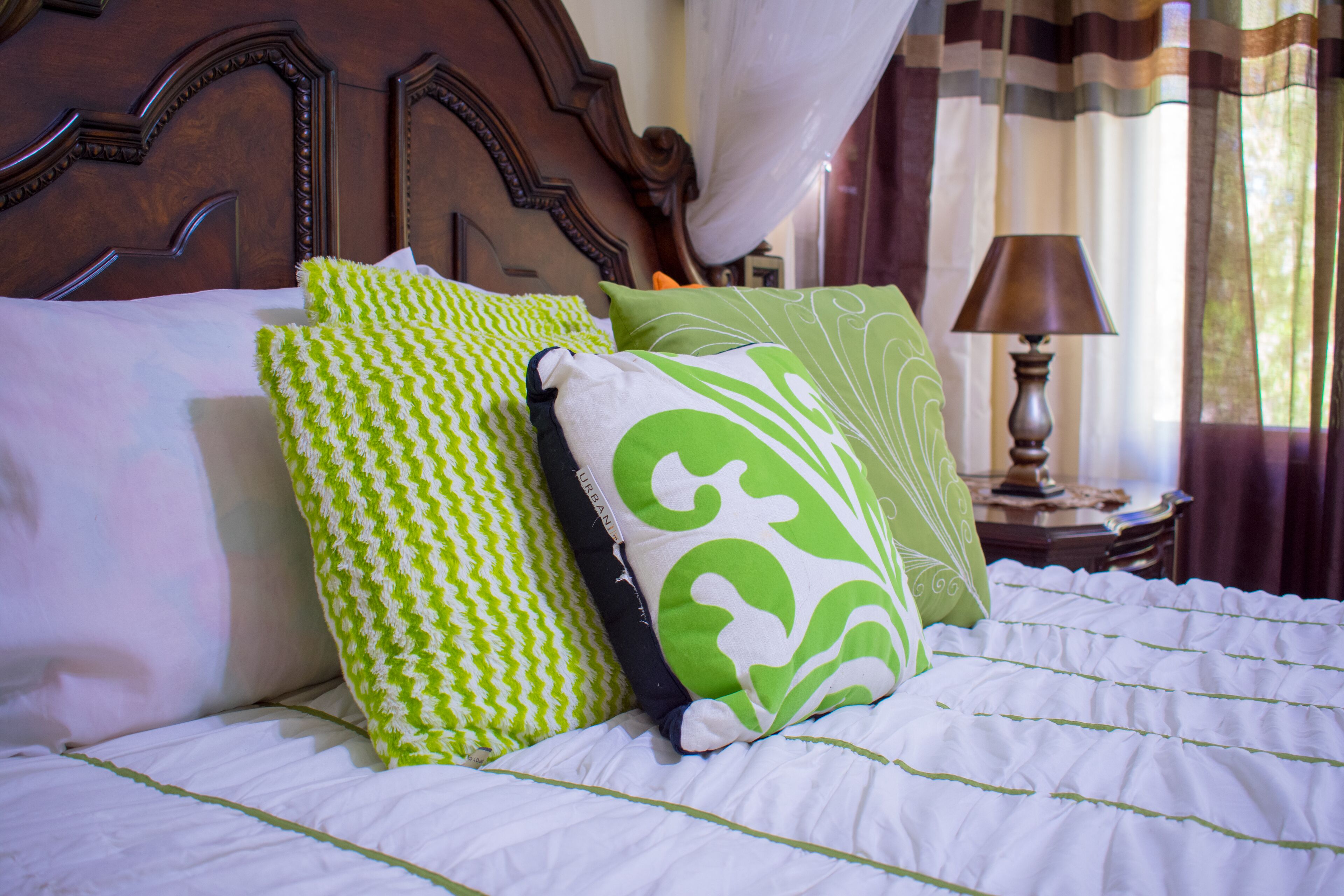 Una cama bien hecha con ropa blanca y varios almohadones de diferentes diseños.