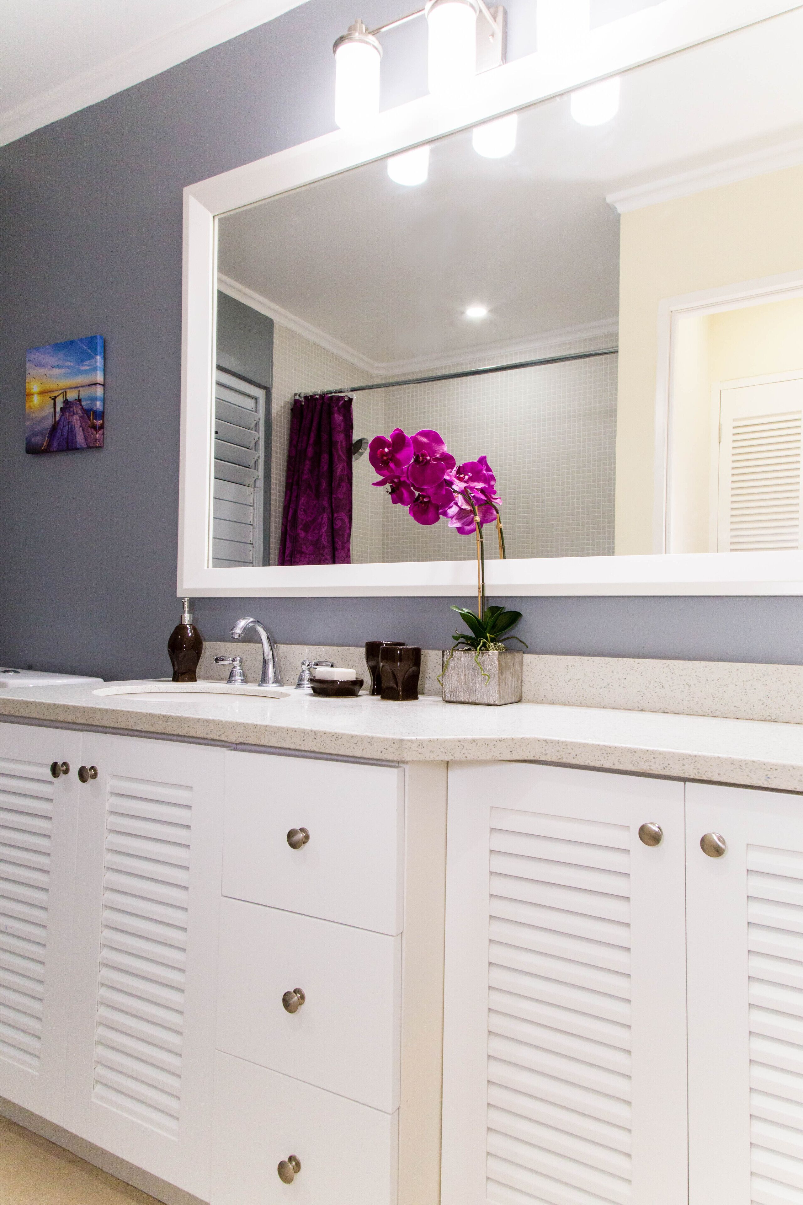 A bathroom with a large mirror, a sink, and a potted orchid.
