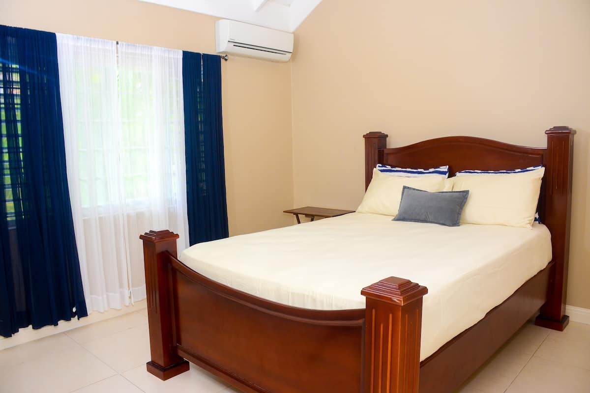 A bedroom with a wooden bed, white bedding, a small bedside table, and a window with blue curtains.