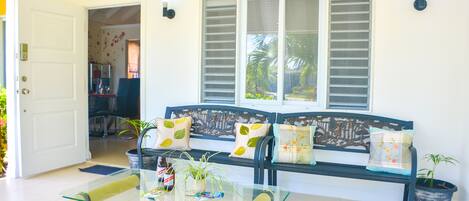 A living room with a glass coffee table, a sofa with patterned cushions, and a large window with shutters.