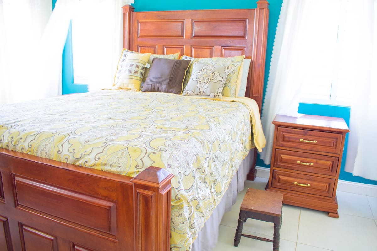 A wooden bed with a patterned bedspread, a nightstand with drawers, and a small wooden stool.