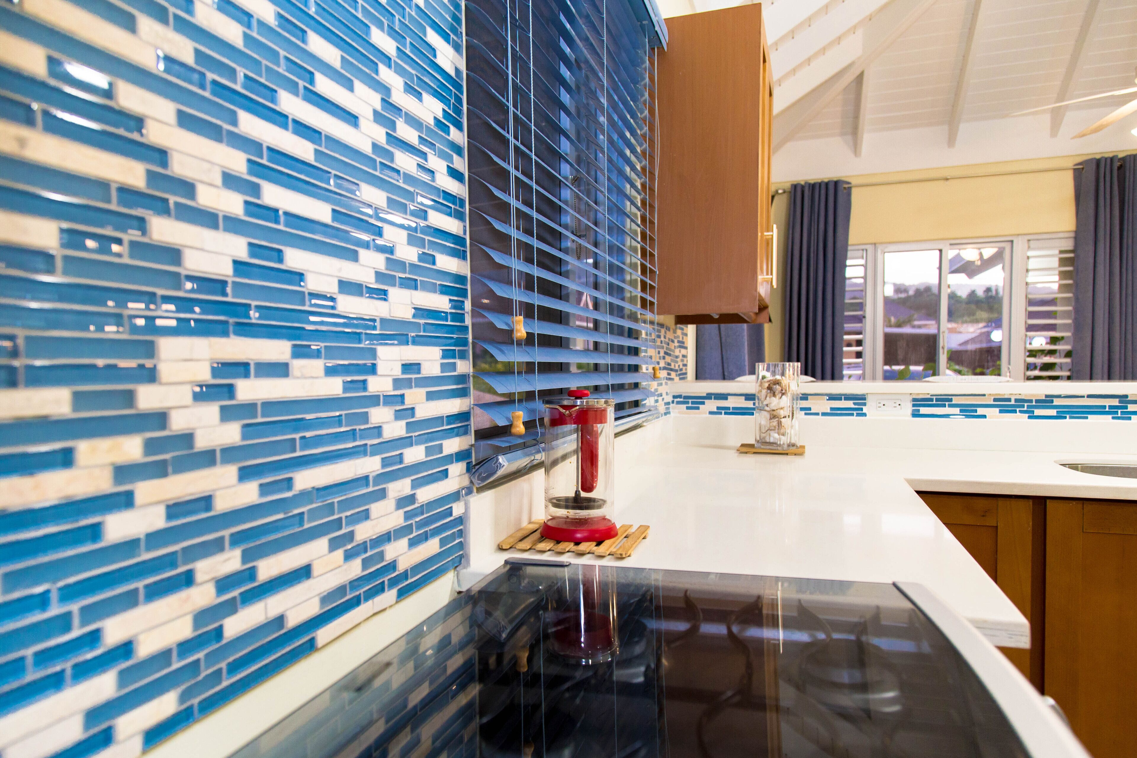 A kitchen with a blue and white tiled backsplash, a black countertop, and a window with curtains.