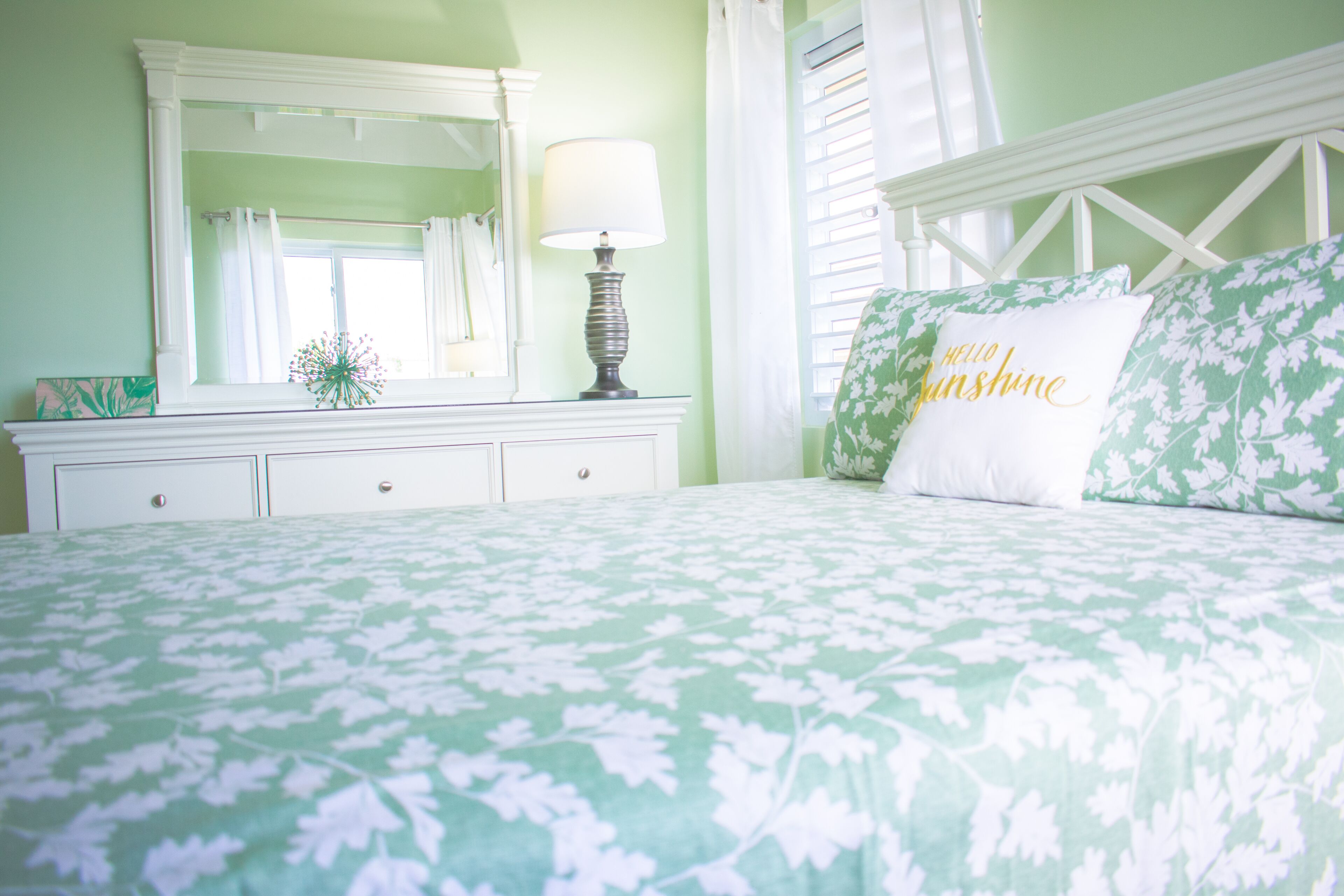 Une chambre à coucher avec une couvre-lit à motifs floraux, une table de chevet avec une lampe, un miroir et une fenêtre avec des rideaux.