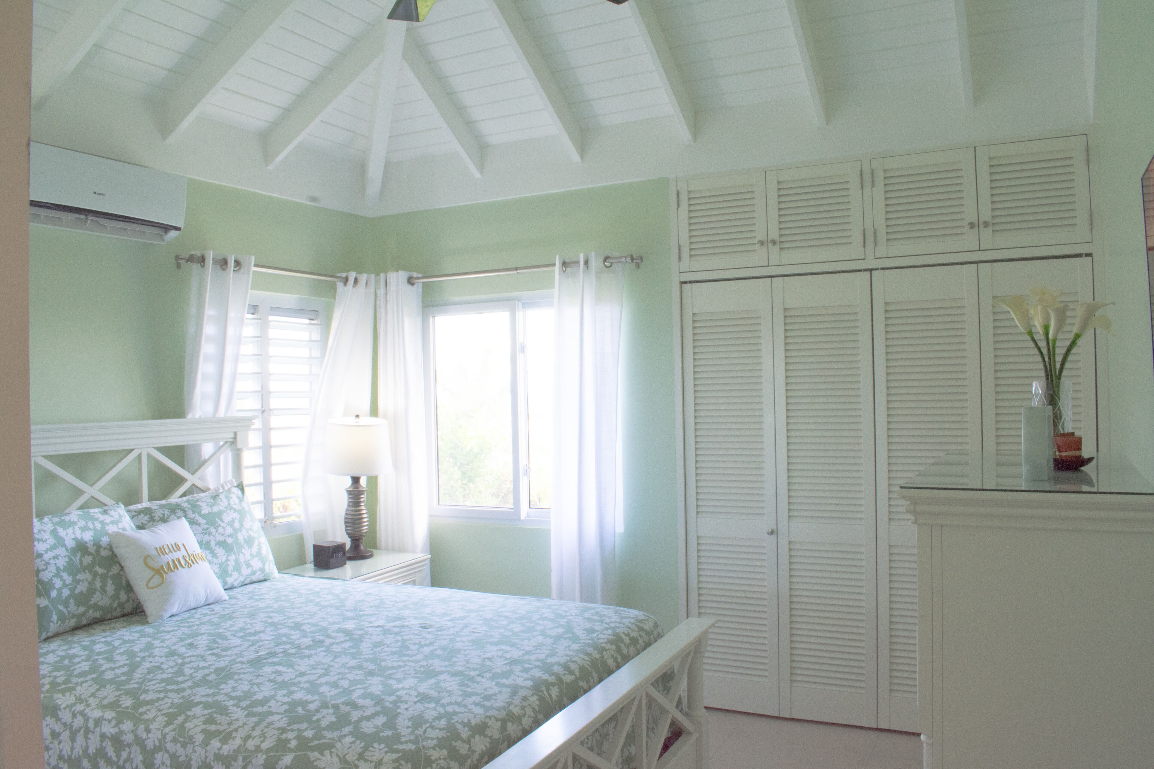 A bedroom with a bed, a nightstand, a lamp, a window with curtains, a wardrobe, and a ceiling fan.