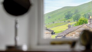 A view through a window of a rural landscape with rolling hills, stone walls, and traditional buildings.