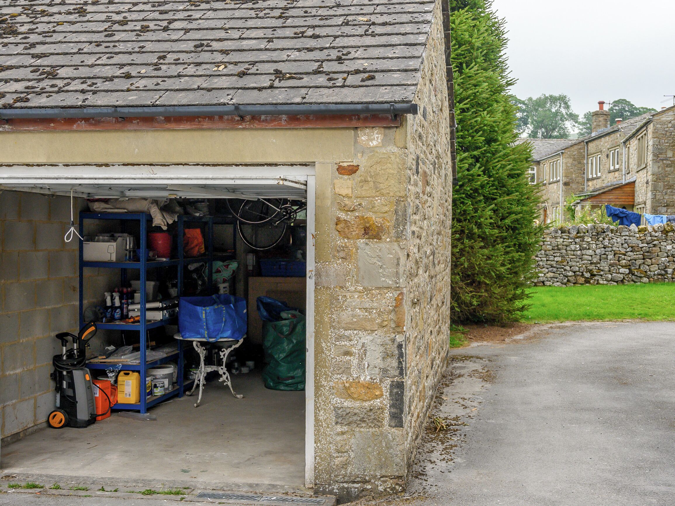 A garage with a blue shelving unit filled with various items, a bicycle, and a lawn mower.