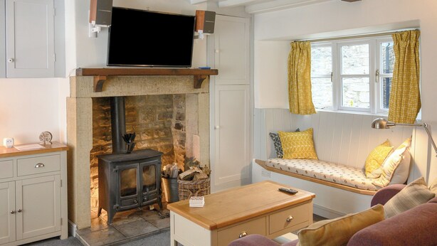 A cozy living room with a stone fireplace, a wooden bench by a window, and a sofa.