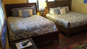 A room with two beds, each with patterned bedding, a small table with a remote control, and a rug.