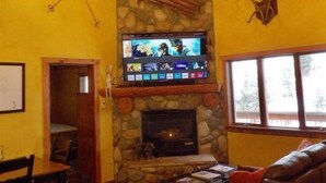 A cozy living room with a stone fireplace, a mounted television, and a leather sofa.