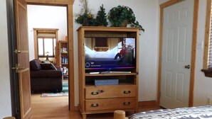 Ett rum med en tv-apparat på ett träställ, en soffa, ett träskåp och en mönstrad matta.