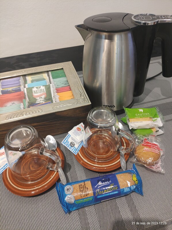 A table with a coffee maker, a glass pitcher, a packet of cookies, and a packet of tea. - Room in homestay (Villa Real)