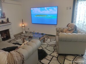 Un salon doté d’un sol imitant le motif de la pierre, d’une table basse en verre, d’une cheminée et d’un téléviseur diffusant des images d’une île tropicale.