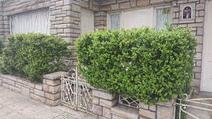 A stone facade with a white door and window shutters, a small statue, and a metal gate. - Room in homestay (Villa Real)
