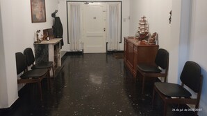 A hallway with a desk, chairs, a cabinet, a door, and a painting on the wall. - Room in homestay (Villa Real)