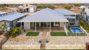 Una casa moderna con un porche cubierto, piscina y jardín ajardinado.