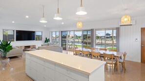 Cozinha moderna com uma ilha grande, área de jantar com cadeiras e vista para uma piscina e casas através de amplas janelas.