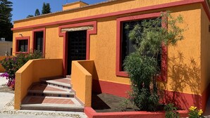 A building with a red door, a small porch, and steps leading to the entrance. - Casa Edilia - Smack in the middle of town/one block from the beach (Los Barriles)