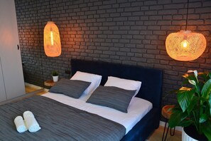 A modern bedroom with a brick wall, a dark headboard, two beds with grey bedding, and hanging light fixtures. - Last Floor Apartment - City Center Old Town / Stare Miasto (Stare Miasto)