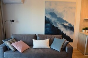 A grey sofa with multiple cushions, a black floor lamp, and a large forest-themed painting on the wall. - Last Floor Apartment - City Center Old Town / Stare Miasto (Stare Miasto)