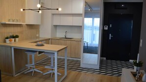 A modern kitchen with a central island, a dining area with bar stools, and a view of a balcony through an open door. - Last Floor Apartment - City Center Old Town / Stare Miasto (Stare Miasto)