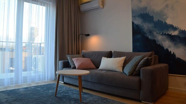 A modern living room with a grey sofa, a round coffee table, and a large painting of a forest. - Last Floor Apartment - City Center Old Town / Stare Miasto (Stare Miasto)