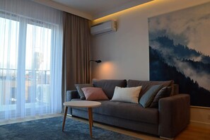 A modern living room with a grey sofa, a round coffee table, and a large painting of a forest. - Last Floor Apartment - City Center Old Town / Stare Miasto (Stare Miasto)
