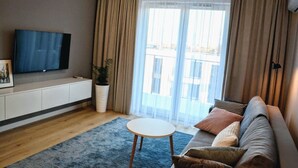 A modern living room with a flat-screen TV, a sofa, a coffee table, and a large window with curtains. - Last Floor Apartment - City Center Old Town / Stare Miasto (Stare Miasto)
