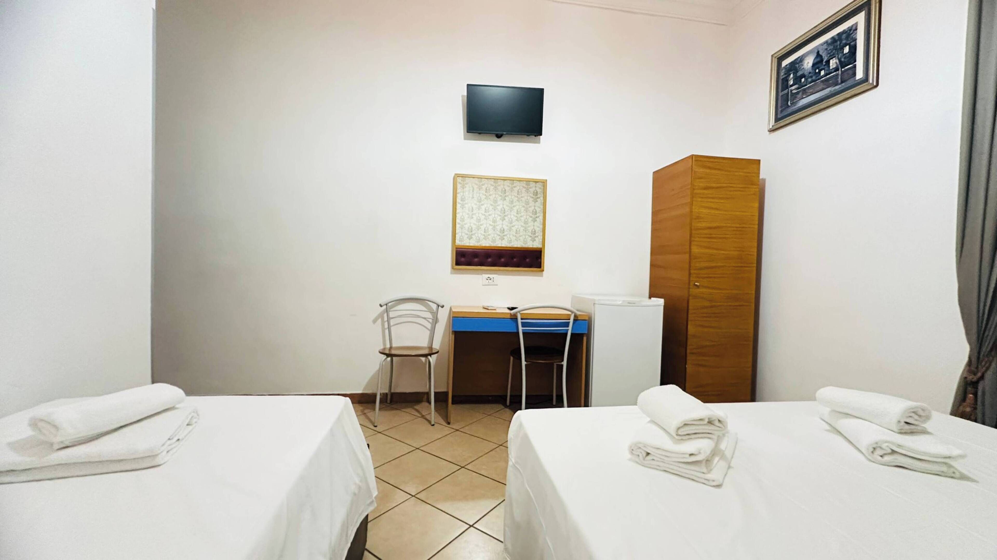 A hotel room with two beds, a desk, a chair, a television, and a wardrobe.
