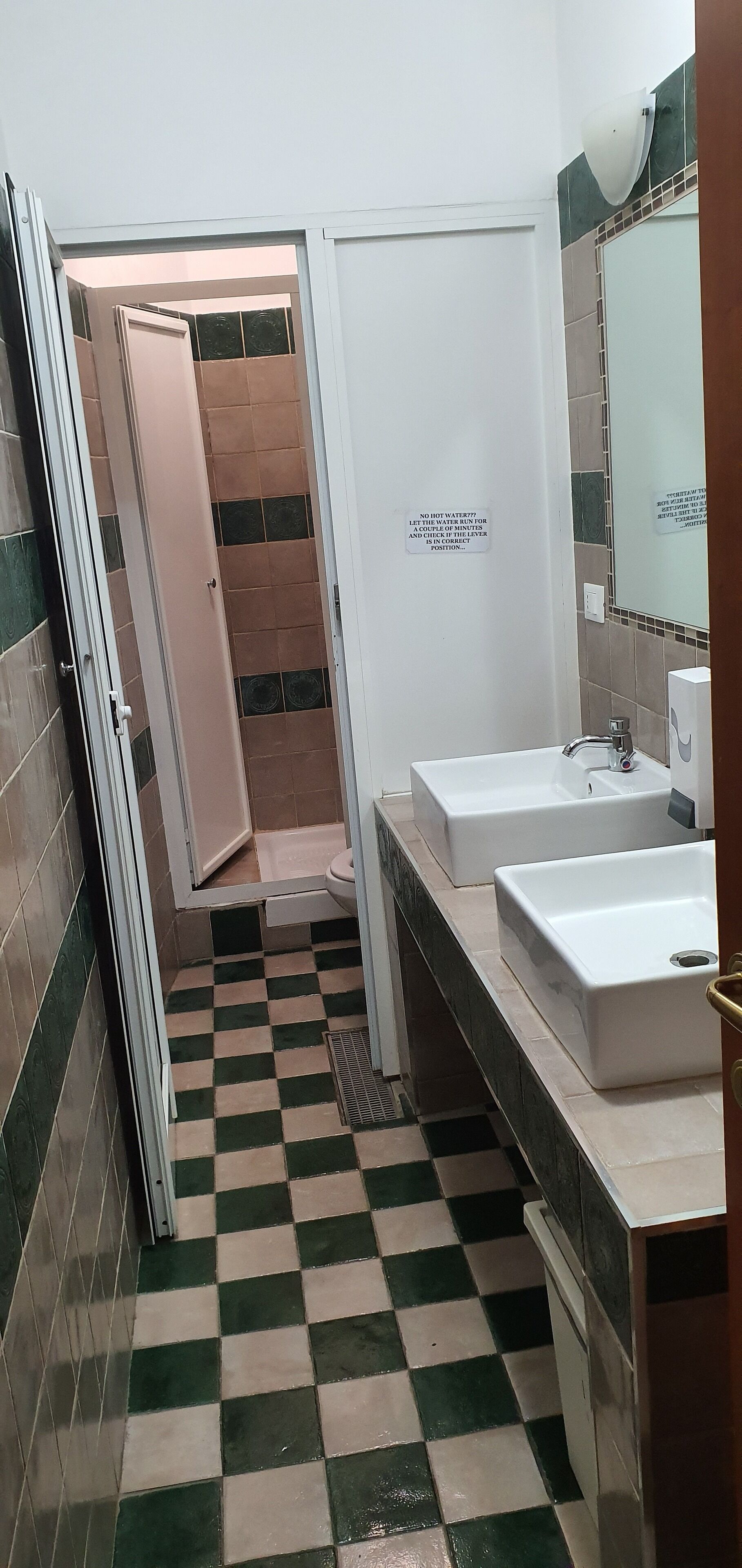A bathroom with a checkered floor, two sinks, a mirror, and a shower stall.