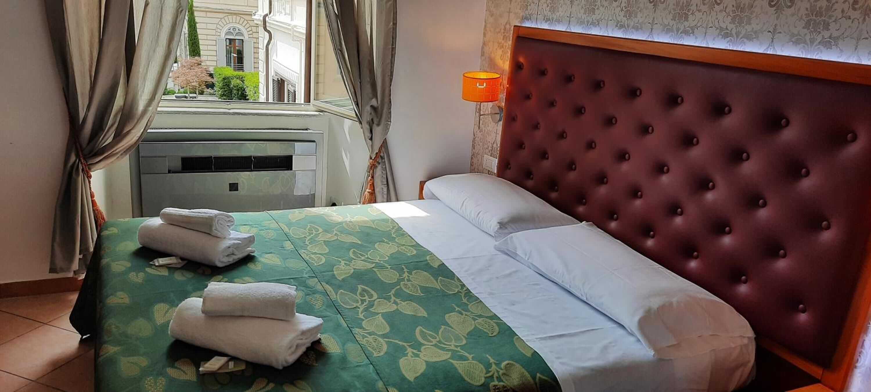 Ein Hotelzimmer mit Bett, Fenster mit Vorhängen, Klimaanlage und Nachttischlampe.