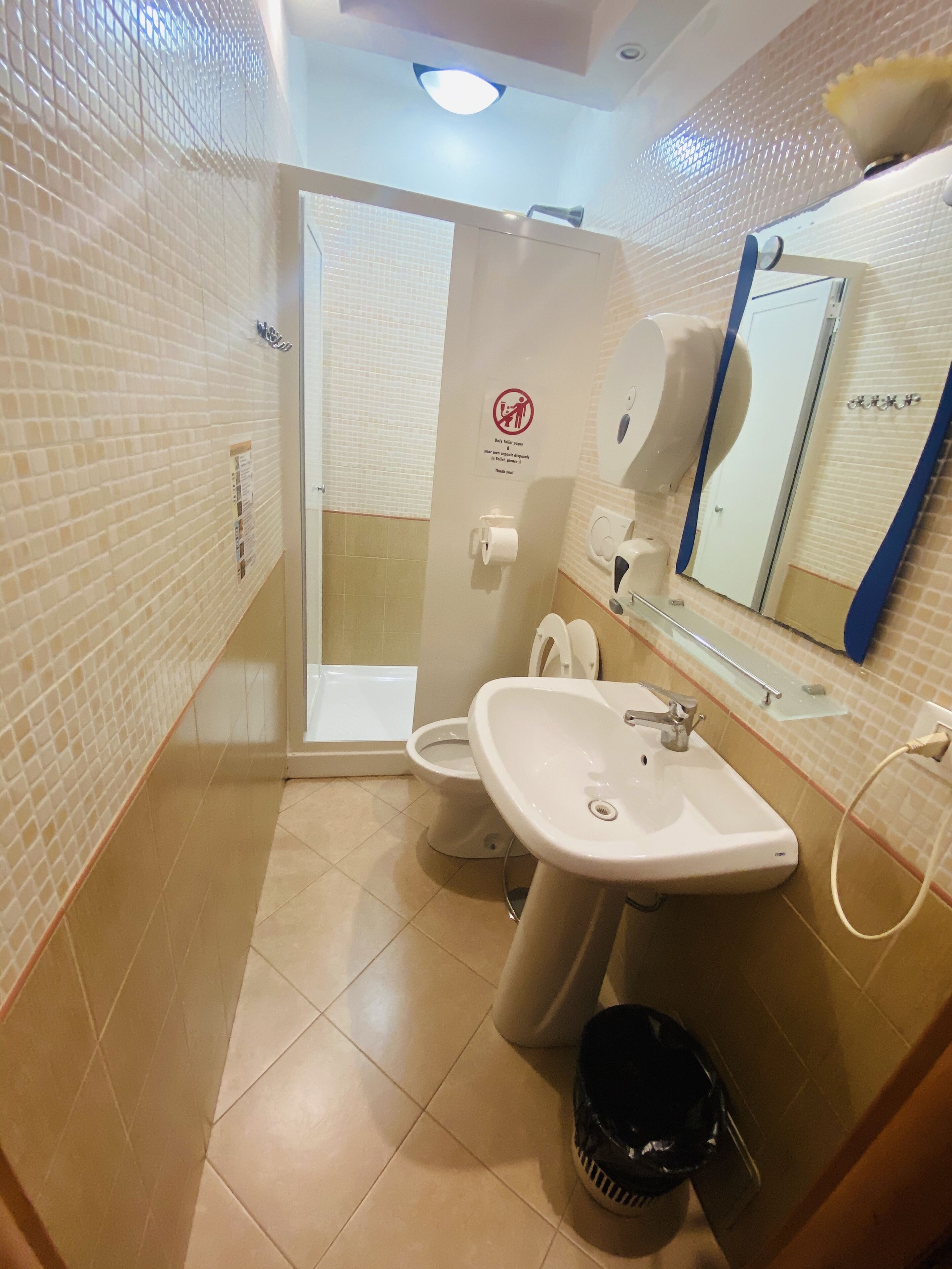 A bathroom with a toilet, sink, and shower. There is a sign indicating no towel drying.