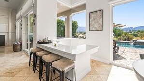 Une cuisine moderne dotée d’un grand îlot central, de tabourets de bar et offrant une vue sur une piscine et des montagnes.