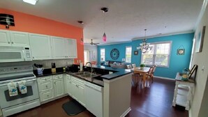 A kitchen with white cabinets, a central island, and a dining area with a table and chairs. - Quick Walk to the Beach!! (North Myrtle Beach)