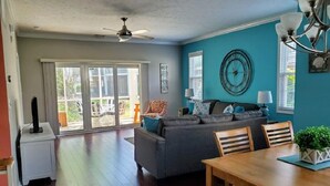 A spacious living room with a grey sofa, a dining table, and a ceiling fan. - Quick Walk to the Beach!! (North Myrtle Beach)