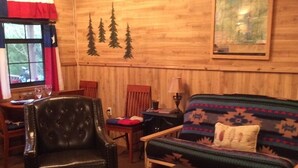 Una sala de estar acogedora con detalles de madera, un sofá, un sillón y una mesita con una lámpara.