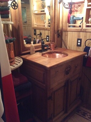 A wooden bathroom with a large sink, a mirror, and a small table with a bottle and a cup. - Private Cabin with hot tub. Nestled in the Woods just off Lake Limestone, Texas. (Jewett)