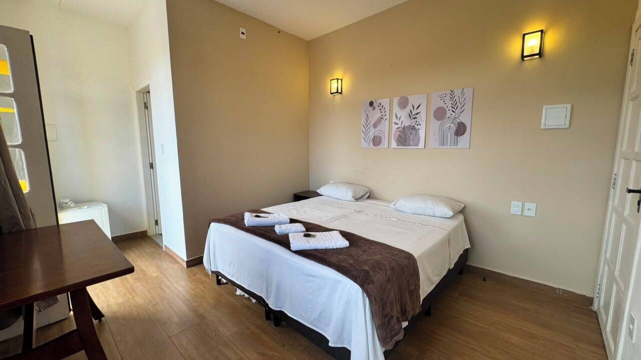 A hotel room with a bed, bedside tables, a desk, and wall-mounted artwork.