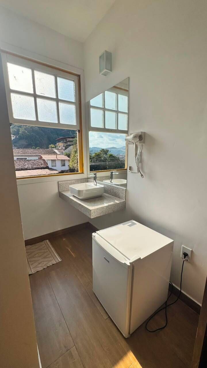 A bathroom with a window, two sinks, a mirror, and a white cabinet.