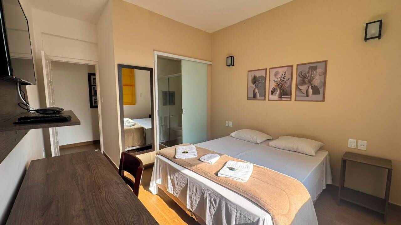 Una habitación de hotel con cama, escritorio, silla, armario y puerta que da a otra estancia.
