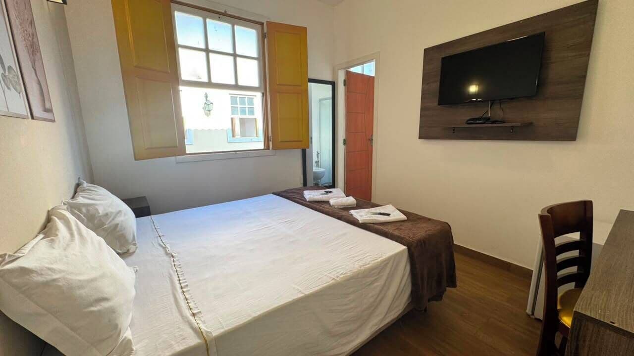 A bedroom with a bed, a television mounted on the wall, and a window with shutters.