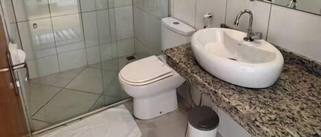 A bathroom with a glass-enclosed shower, a white toilet, a sink with a granite countertop, and a mirror above the sink.